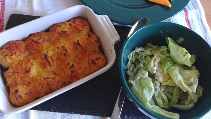 Ein gebackener Cottage Pie in einer wei&szlig;en Auflaufform neben einer Sch&uuml;ssel Salat.