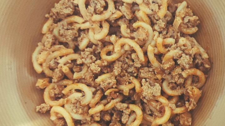 Ein Teller mit Hackfleisch und lockigen Nudeln, die in einer beige-braunen Keramiksch&uuml;ssel serviert werden.