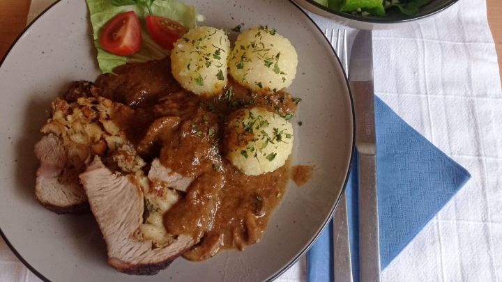 Ein Teller mit gef&uuml;lltem Kalbsbraten, Kn&ouml;deln und So&szlig;e, dekoriert mit Petersilie. Daneben eine Sch&uuml;ssel Salat.