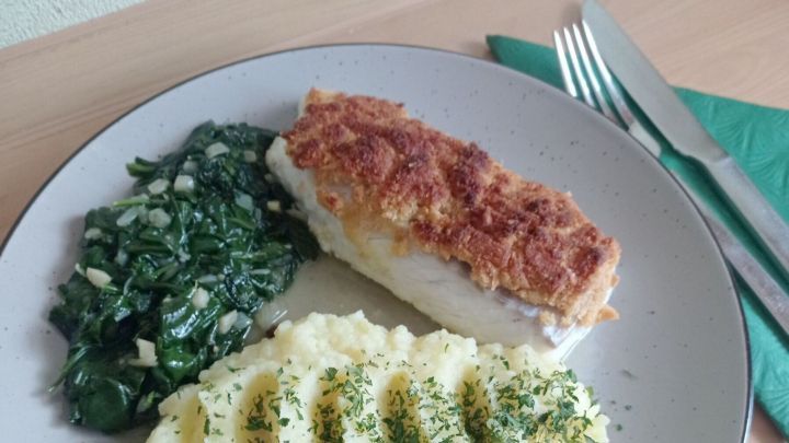 Das Kabeljaufilet mit Parmesankruste, Blattspinat und Kartoffelp&uuml;ree auf angew&auml;rmtem Teller angerichtet.