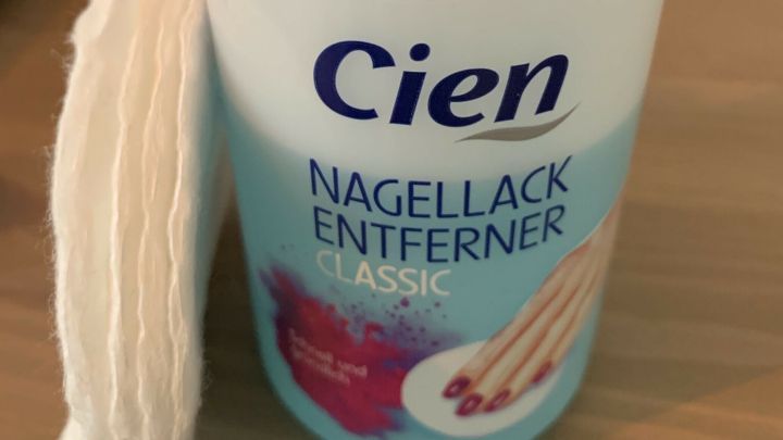 Ein Fläschchen Nagellackentferner steht neben einem Wattepad auf einem Tisch. Es wird zur Entfernung von getrocknetem Lack verwendet.