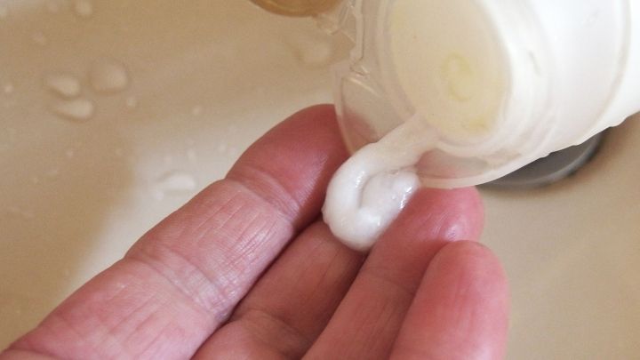 Eine Hand h&auml;lt eine fl&uuml;ssige Sp&uuml;lung, die aus einer Flasche flie&szlig;t, w&auml;hrend sie &uuml;ber einem Waschbecken steht.