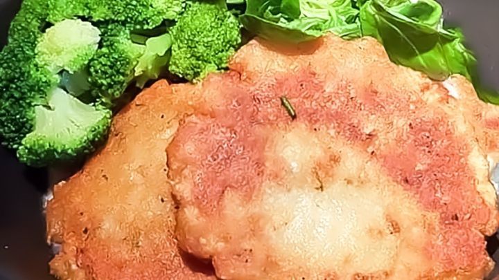 Drei goldbraun panierte Veganer:innenburger liegen neben frischem Brokkoli und gr&uuml;ner Salat in einer Sch&uuml;ssel.