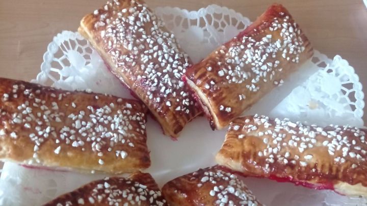 Johannisbeer-Bl&auml;tterteigtaschen: Knuspriger Genuss mit fruchtiger F&uuml;llung, perfekt serviert auf einem dekorativen Tortenspitzenpapier.