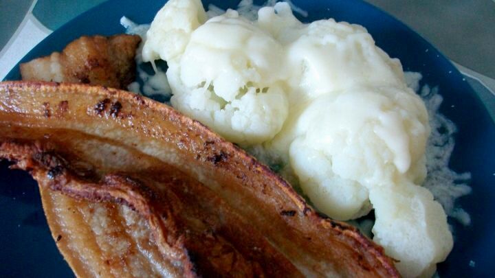 Blumenkohl mit zerlassener Butter &uuml;bergossen und zwei leckere, kr&auml;ftig angebratene Schweinebauchscheiben.