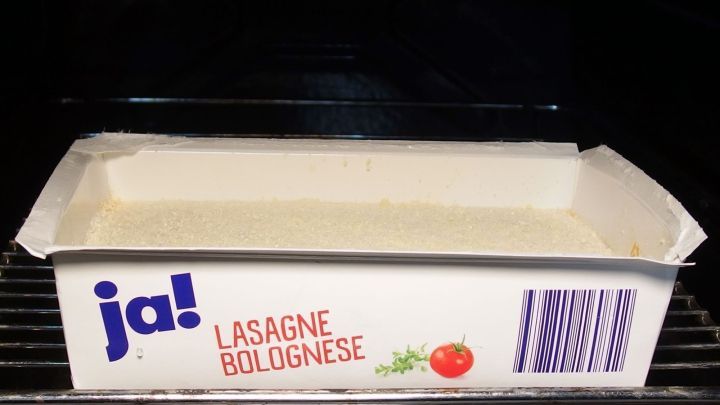 Eine Tiefk&uuml;hl-Lasagne in einer Verpackung steht im Ofen, bereit zum Backen in einer dunklen Umgebung.