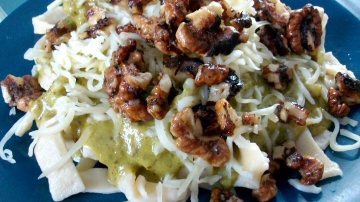 Bandnudeln mit Pesto und Waln&uuml;ssen: Auf dem Teller siehst Du breite Nudeln mit gr&uuml;nem Pesto, ger&ouml;steten Waln&uuml;ssen und K&auml;se.