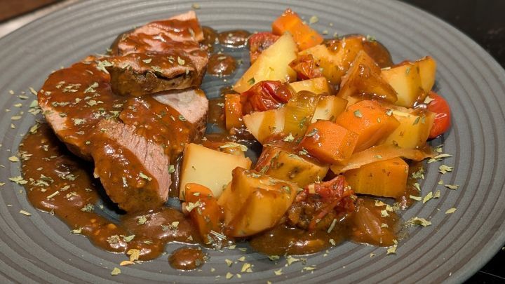 Schinkenbraten auf Kartoffel-Gem&uuml;sebett: Saftige Bratenscheiben mit dunkler So&szlig;e, dazu Kartoffeln, Karotten und Tomaten aus dem Ofen.