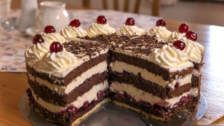 Eine Schwarzw&auml;lder Kirschtorte steht angeschnitten auf einem Tisch. Sie zeigt mehrere Schichten aus Schokolade, Sahne und Kirschen.