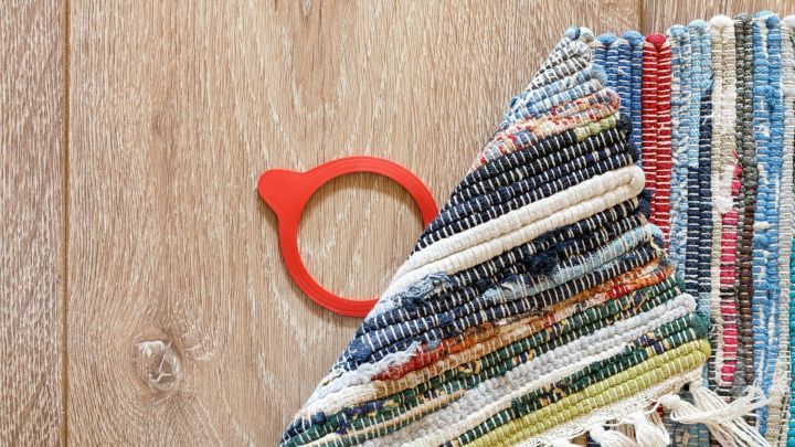 Ein Teppich liegt teilweise auf dem Boden, w&auml;hrend ein roter Teppichclip den Rutschschutz unterst&uuml;tzt und Stabilit&auml;t bietet.