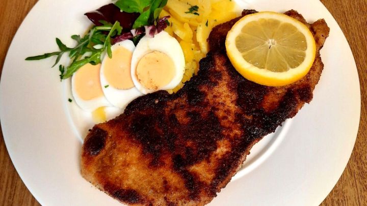 Ohne Mehl paniertes Schweineschnitzel appetitlich angerichtet mit Kartoffelsalat, Zitrone, gekochten Ei-Scheiben und etwas Rucola.