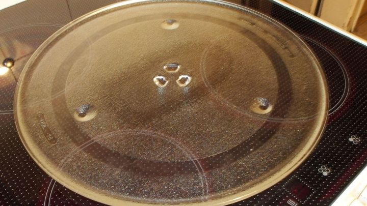 Ein runder Teller aus einer alten Mikrowelle liegt auf einer modernen Kochplatte, bereit zur weiteren Nutzung in der K&uuml;che.