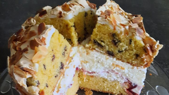 Preiselbeer-Baiser-Torte mit heller Cremef&uuml;llung, luftigem Baiser und Mandelbl&auml;ttchen auf einer Glasplatte.