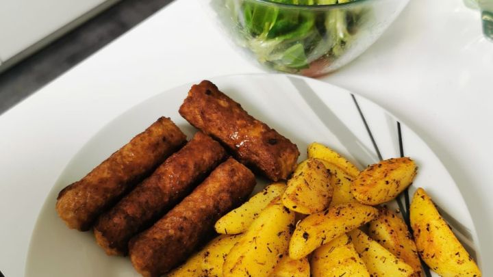 Cevapcici mit pikanten Kartoffelspalten und Feldsalat mit Datteltomaten an Senf-Honig Dressing serviert.