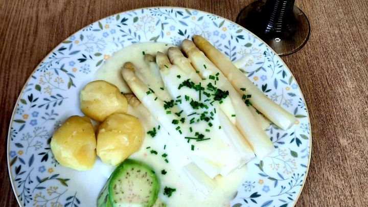Wei&szlig;er Spargel mit kalorienarmer Spargel So&szlig;e, dazu Kartoffeln, Avocado und Schnittlauchringe auf floralem Teller mit Glas Wei&szlig;wein
