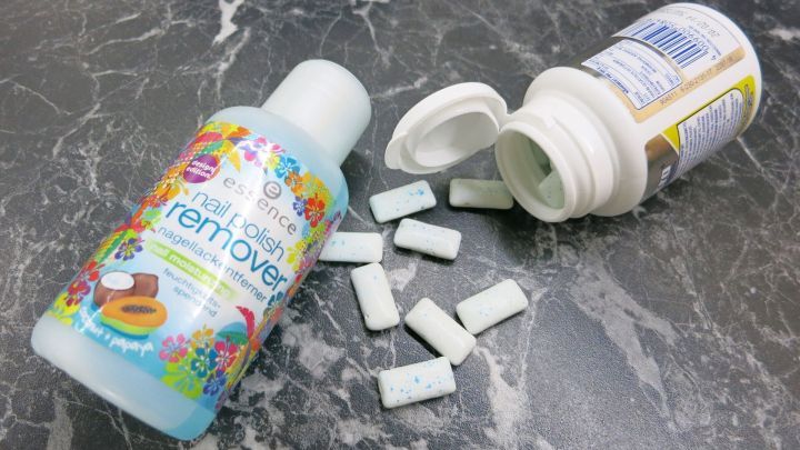 Ein Fl&auml;schchen Nagellackentferner steht auf einer Marmoroberfl&auml;che neben Kaugummist&uuml;cken, die verstreut liegen.