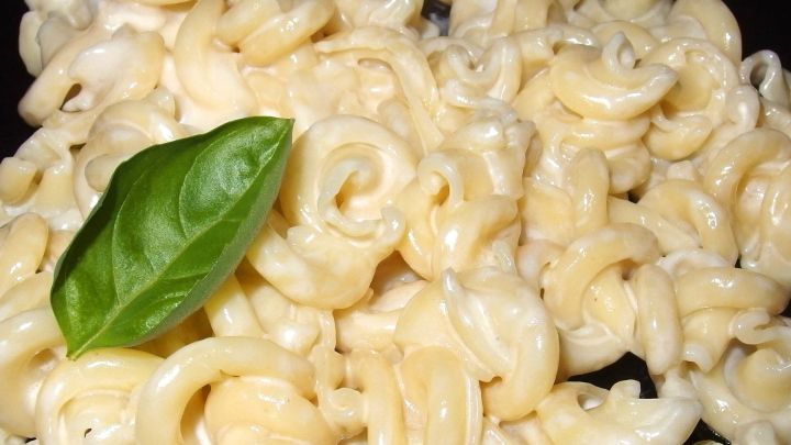 Zarte Nudeln liegen in einer schwarzen Sch&uuml;ssel, garniert mit einem frischen Basilikumblatt, bereit f&uuml;r Fertigsaucen.