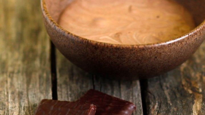 Eine Holzschale mit Pfefferminz-Schokoladent&auml;felchen-Creme steht auf einem rustikalen Holztisch, daneben liegen zwei Schokoladent&auml;felchen.