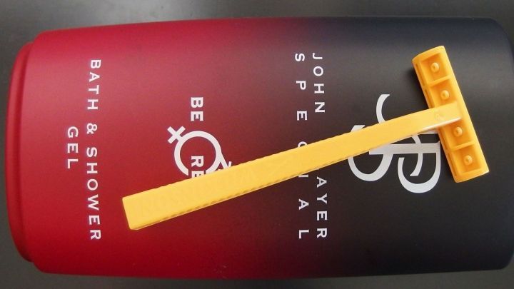 Ein Duschgelbeh&auml;lter mit einem Rasierer liegt darauf. Der Hintergrund ist einfarbig schwarz.