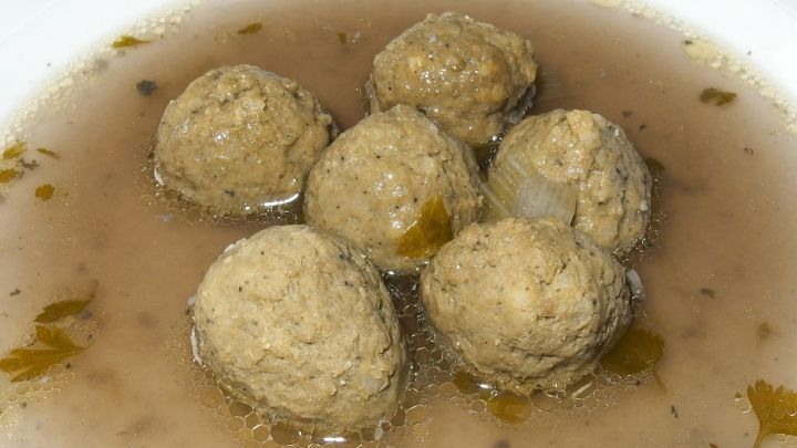 In einer Sch&uuml;ssel schwimmen mehrere Leberkn&ouml;del in einer klaren Br&uuml;he, umgeben von gr&uuml;nen Kr&auml;utern f&uuml;r zus&auml;tzlichen Geschmack.