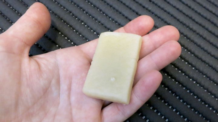 Eine Hand h&auml;lt ein St&uuml;ck Gallseife &uuml;ber einem dunklen, gerippten Hintergrund.