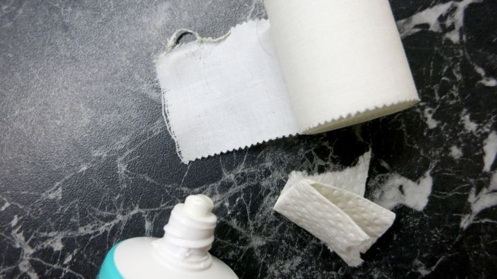 Eine Tube Sole-Zahncreme steht auf einer dunklen Marmoroberfl&auml;che, daneben liegen Streifen eines wei&szlig;en Pflasters.