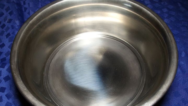 Eine gl&auml;nzende Edelstahlsch&uuml;ssel steht auf einem blauen Tuch und reflektiert das Licht, zeigt ihre Sauberkeit und Pflege.