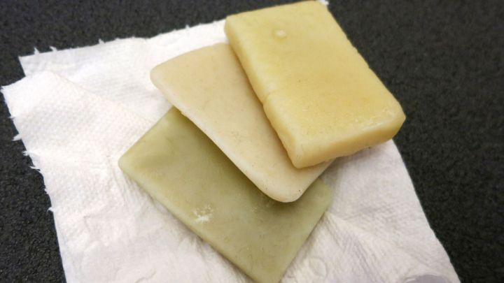 Drei Seifenreste liegen auf einem Papiertuch auf dunklem Untergrund, trocken und sichtbar abgenutzt.