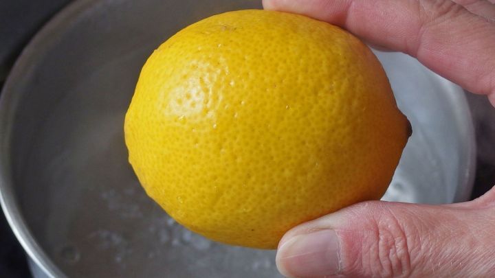 Eine hand h&auml;lt eine gelbe Zitrone &uuml;ber einen Topf mit kochendem Wasser, um die harte Zitrone weich zu machen.