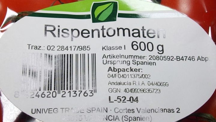 Eine Beschriftung zeigt frische Rispentomaten mit einem Gewicht von 600 g, verpackt in einer Supermarktumgebung.