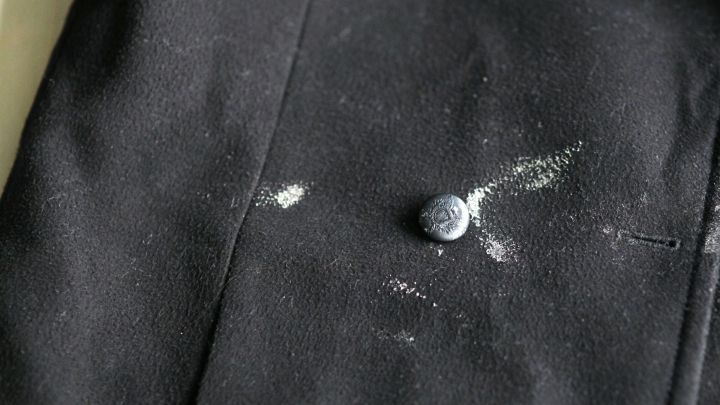 Dunkler Stoff zeigt mit Flecken, w&auml;hrend eine Hand vorsichtig die angetrockneten R&uuml;ckst&auml;nde wegrubbelt.