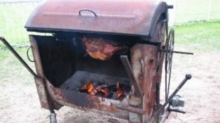 Ein robuster Grill rostet leicht, w&auml;hrend Fleisch &uuml;ber offenem Feuer br&auml;t; auf einer Rasenfl&auml;che im Freien.