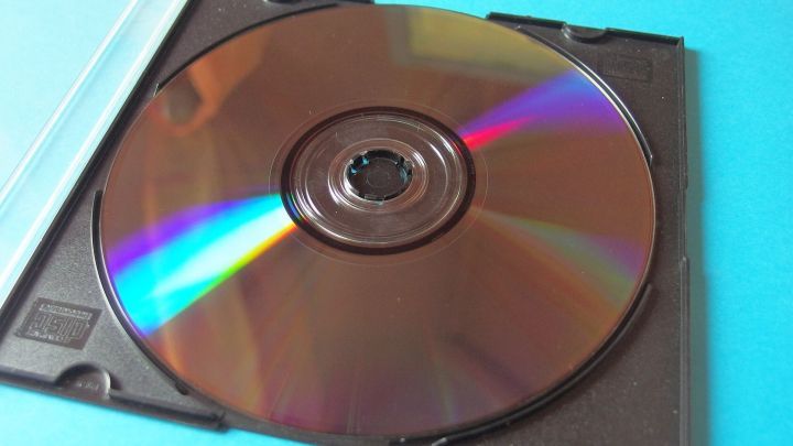 CD-RW in einer schwarzen Kunststoffh&uuml;lle, auf blauem Hintergrund liegend, zeigt regenbogenartige Reflexionen.