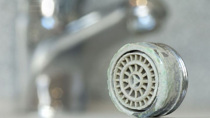 Ein entkalkter Perlator liegt vor einem Wasserhahn, um Drainageprobleme zu beheben. Der Hintergrund ist unscharf.