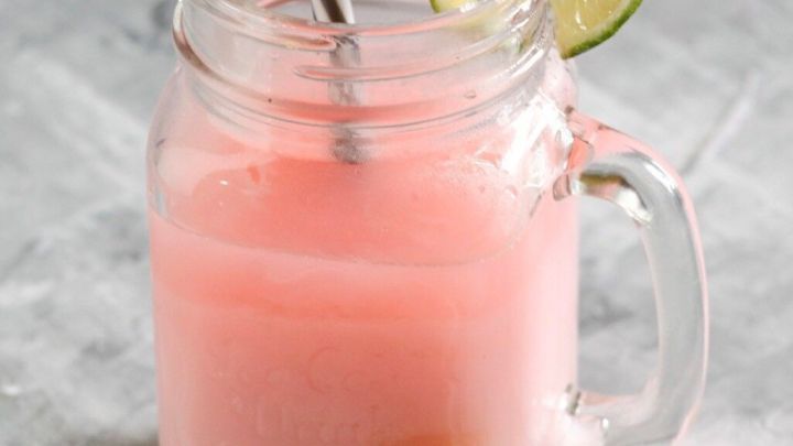 Ein Glas Joghurtdrink mit einem Strohhalm steht auf einem grauen Hintergrund. Limettenscheiben liegen daneben.