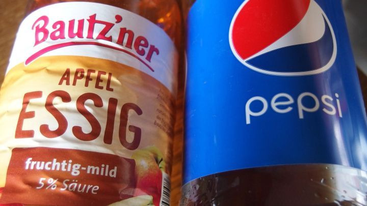 Eine Flasche Apfelessig und eine Pepsi-Flasche stehen nebeneinander, bereit zur Anwendung gegen Ablagerungen im Klo.