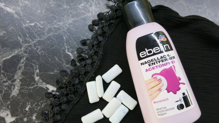 Ein Fl&auml;schchen Nagellackentferner liegt neben mehreren Kaugummiresten auf einer schwarzen Oberfl&auml;che mit einer dezenten Textur.