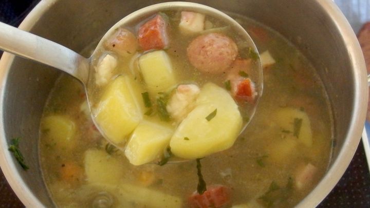 Eine Suppenkelle sch&ouml;pft eine herzhafte T&uuml;tensuppe mit Kartoffeln und Gem&uuml;se aus einem gro&szlig;en Topf.