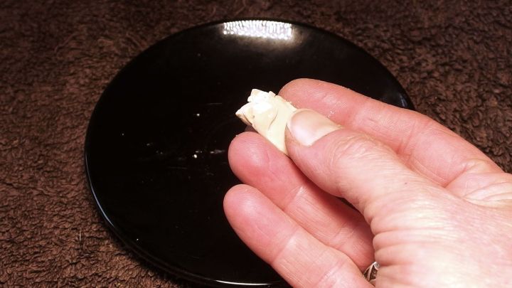 Eine Hand h&auml;lt ein kleines St&uuml;ck Hefe &uuml;ber einem schwarzen Teller, w&auml;hrend es auf einer dunklen Oberfl&auml;che steht.