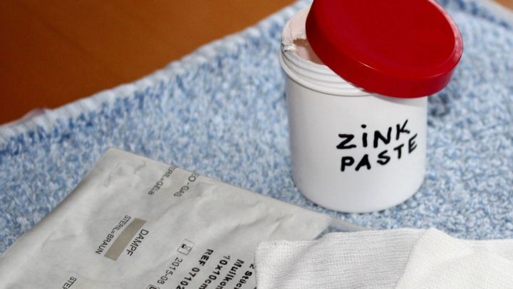 Eine Zinkpaste-Dose mit rotem Deckel steht auf einem Handtuch, umgeben von einem Rezept und einem weiteren Tuch.