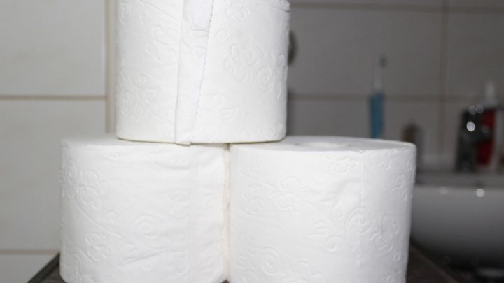 Drei Toilettenpapierrollen stehen stabil auf einem Tisch im Badezimmer, was auf den Umgang mit Durchfall hinweist.