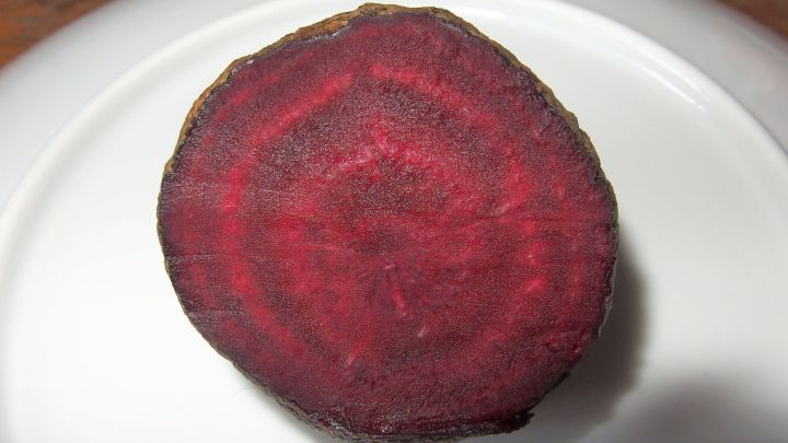 Eine rote Bete liegt auf einem wei&szlig;en Teller, bereit zum F&auml;rben von Shirts. Ihre leuchtend rote Farbe zeigt die nat&uuml;rliche F&auml;rbemethode.