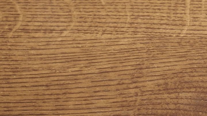 Eine h&ouml;lzerne Oberfl&auml;che zeigt feine, dunkle Holzmaserungen in einem warmen Braunton, mit leichten, unregelm&auml;&szlig;igen Flecken.