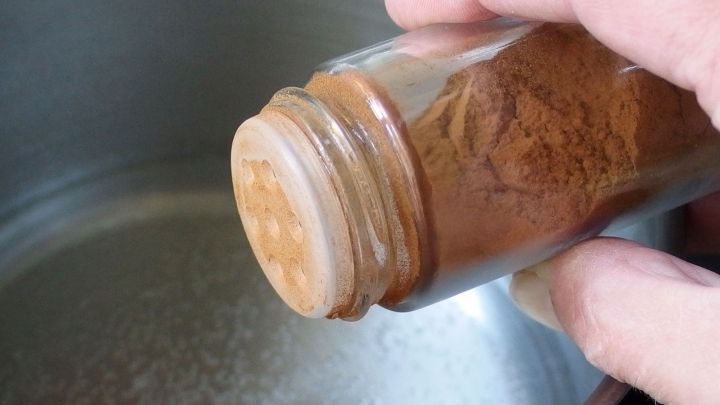 Eine Hand h&auml;lt ein Glas mit Zimt &uuml;ber einem Topf, w&auml;hrend das Gew&uuml;rz gew&auml;rmt wird, um Kochger&uuml;che zu neutralisieren.