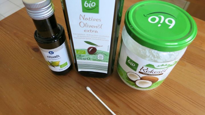 Eine Flasche mit &Ouml;l, eine Dose mit einer Creme und ein Wattest&auml;bchen liegen auf einem Holztisch, bereit zur Anwendung gegen Schnupfen.