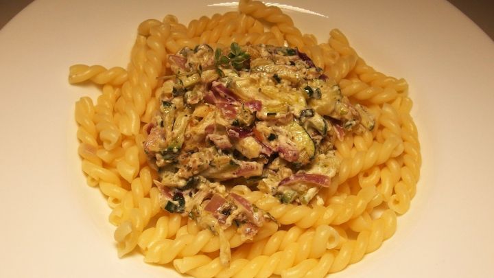Nudeln mit Zucchini-So&szlig;e liegen halbkreisf&ouml;rmig auf einem Teller, bedeckt mit einer cremigen So&szlig;e und Kr&auml;utern.