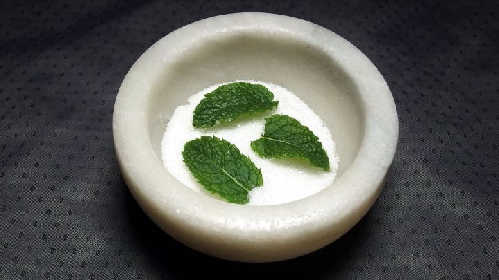 Eine Sch&uuml;ssel mit Minzbl&auml;ttern schwimmt in einer cremigen, s&uuml;&szlig;en So&szlig;e auf einem dunklen Untergrund.