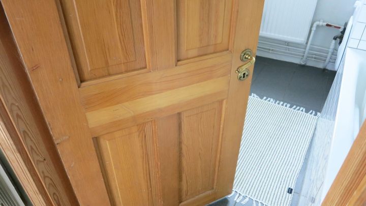 Eine Holzt&uuml;r steht ge&ouml;ffnet im Raum, w&auml;hrend das Licht den Holzton betont und die Umgebung hell erleuchtet.