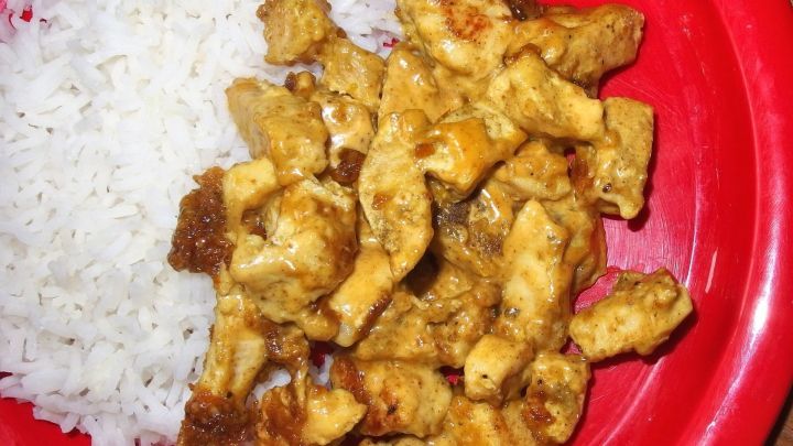 Leckeres Curry-Geschnetzeltes liegt saftig auf einem roten Teller neben fluffigem Reis in einer einfachen K&uuml;che.