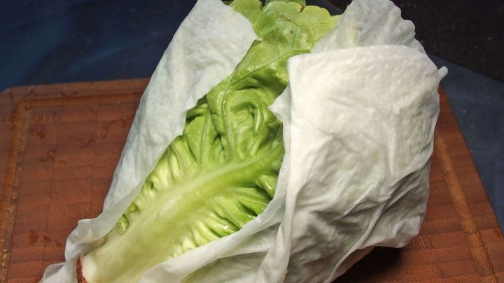 Frischer Salat liegt auf einem Holzbrett, eingewickelt in ein feuchtes Tuch, um knackig zu bleiben.